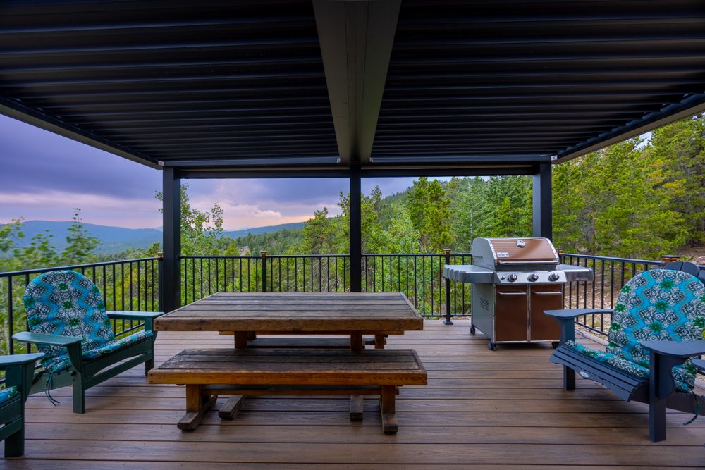 A deck with a motorized pergola and outdoor kitchen