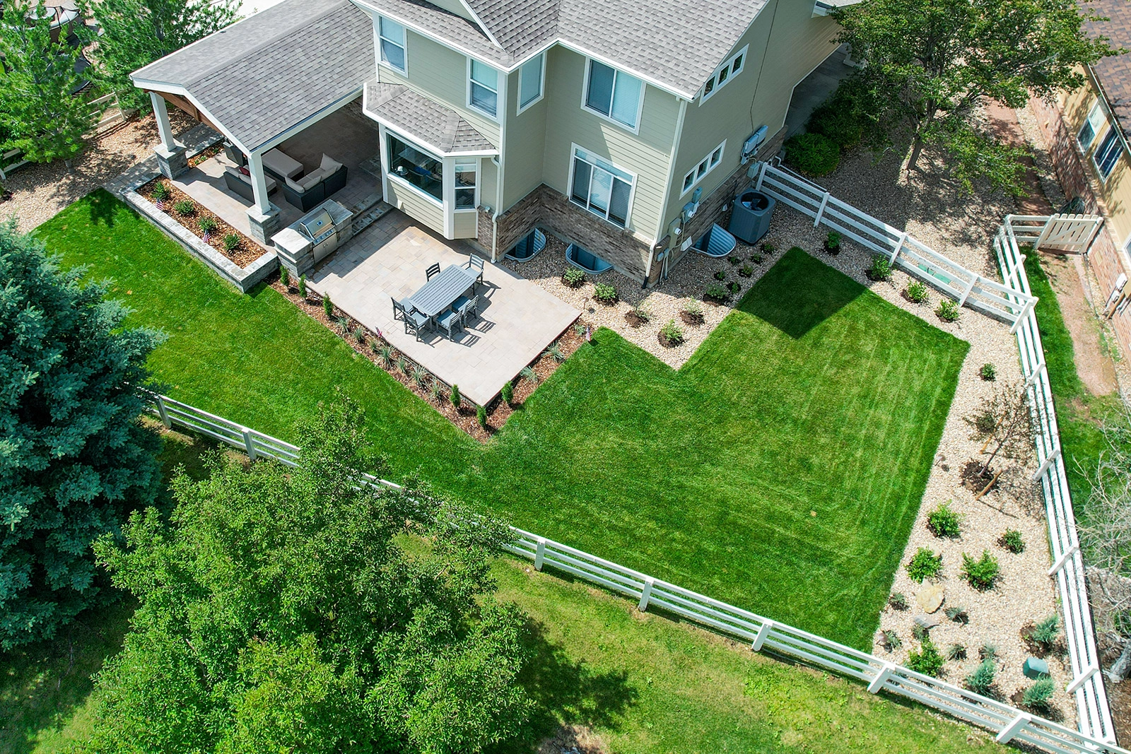 Aerial view of a landscaped backyard with lawn, paver patio, and covered structure