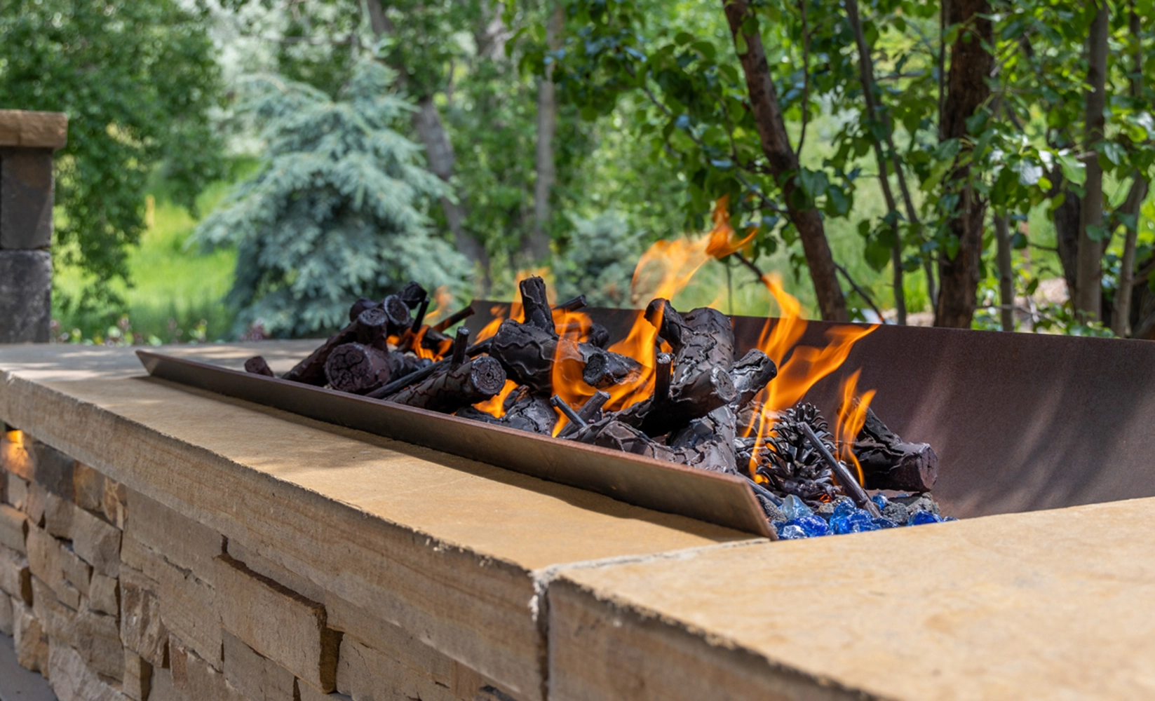 Linear gas fire pit set into a stone wall with flames and glass media